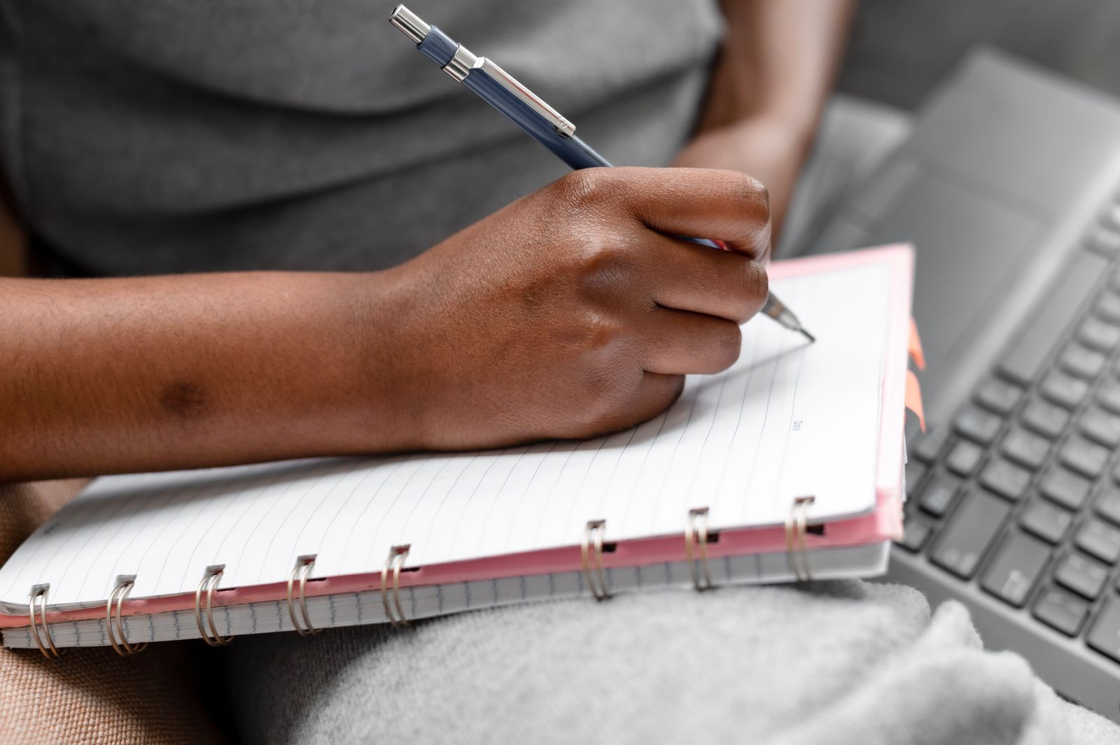 A person taking handwritten notes beside a laptop